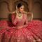 Hot Pink Rani Pink lehenga choli set with heavy gold zari and shisha mirror work worn by a model in a traditional seated pose. Styled with an elaborate Polki and emerald choker necklace, jhumkas, maang tikka, and gajra-adorned bun.